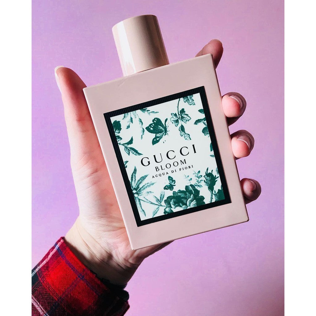 Hand holding a Gucci Bloom perfume bottle against a purple background Gucci Bloom Acqua Di Fiori Eau de Toilette 100 ml (3.4 fl.oz)