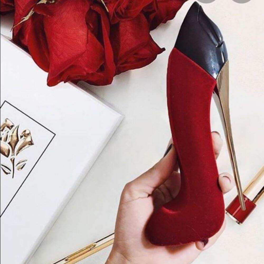 Red high-heeled shoe held by a hand with red roses and a box in the background