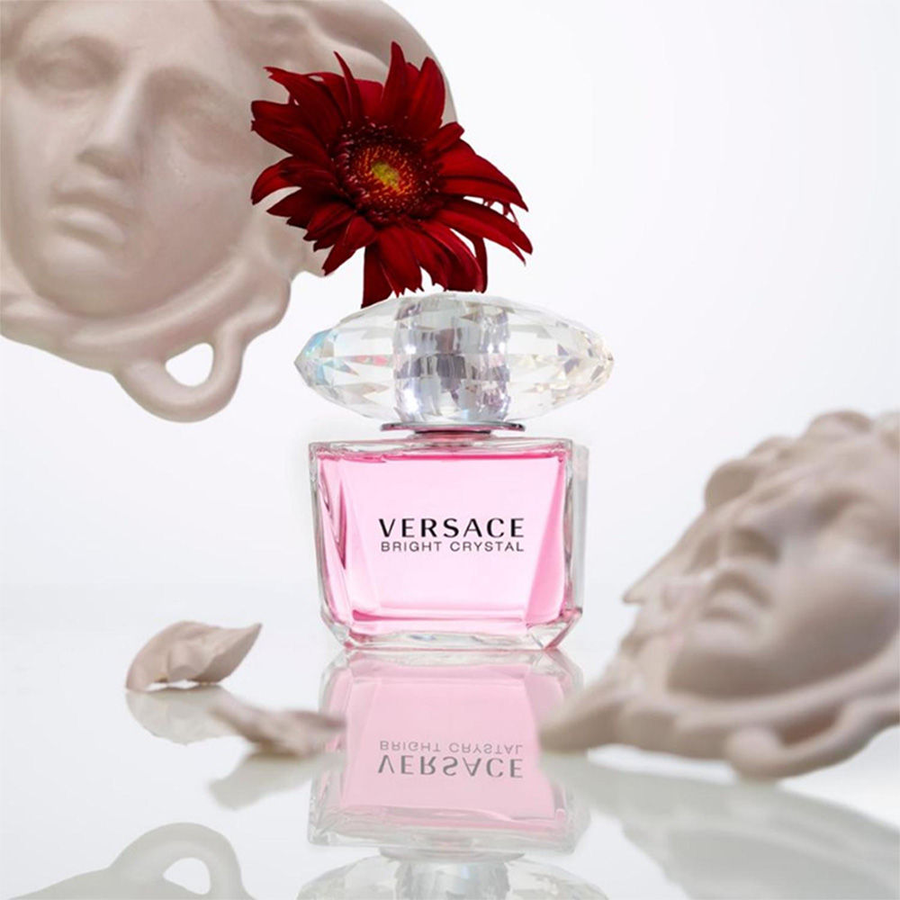 Versace Bright Crystal perfume bottle with a red flower on a reflective surface.