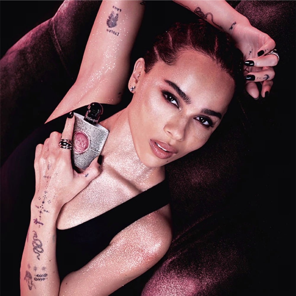 Woman with glittery makeup and tattoos holding a phone case against a dark background
