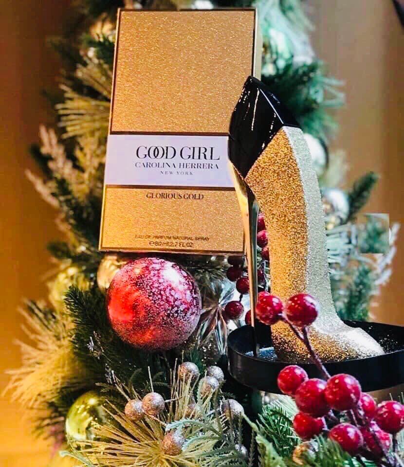 Gold Carolina Herrera perfume box with a decorative shoe and Christmas tree in the background
