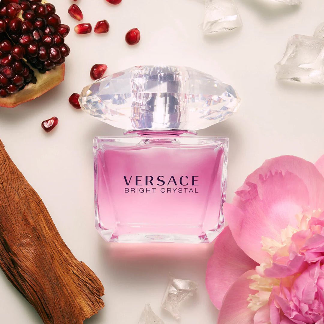 Versace Bright Crystal perfume bottle with pomegranate, flowers, and ice cubes on a white background