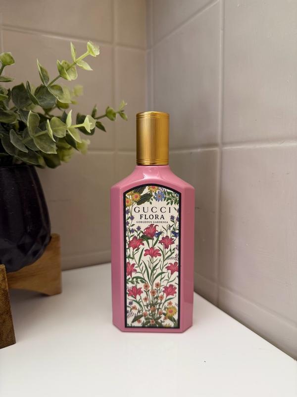 Pink Gucci Flora bottle with floral design on a white surface with a plant in the background.