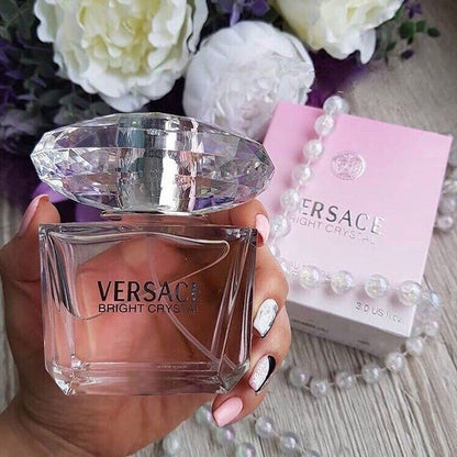 Versace perfume bottle held by a hand with flowers and packaging in the background