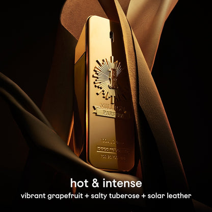 Gold perfume bottle with brand logo, draped in fabric on a dark background
