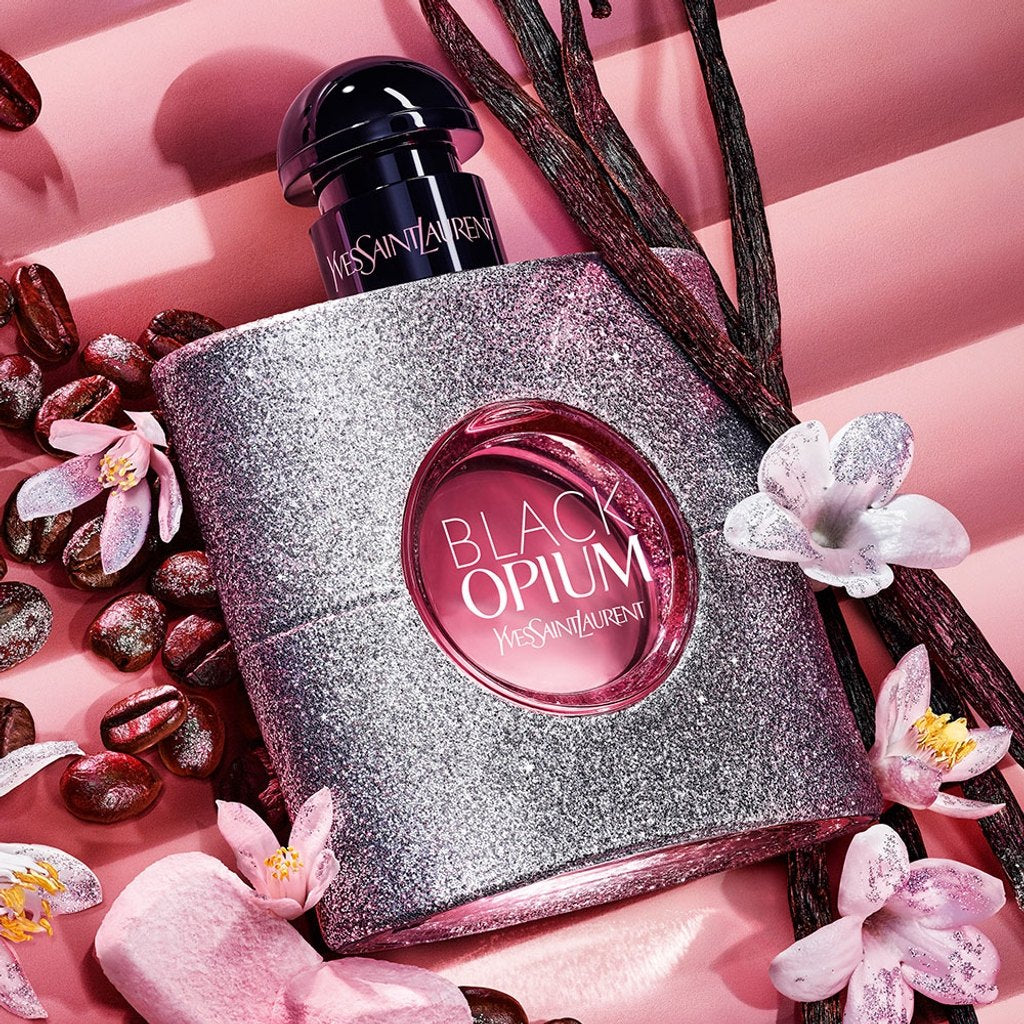YSL Black Opium perfume bottle with flowers and vanilla beans on a pink background