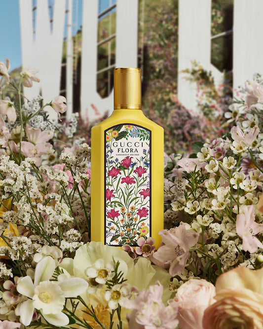 Gucci Flora perfume bottle surrounded by flowers with a white picket fence in the background