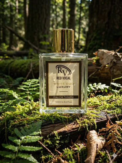 Perfume bottle labeled 'Red Vocal' on a forest floor with trees and foliage in the background Red Vocal White Oud Luxury Premium Perfume Eau De Toilette – Unisex 100ml Bold & Long-Lasting Fragrance