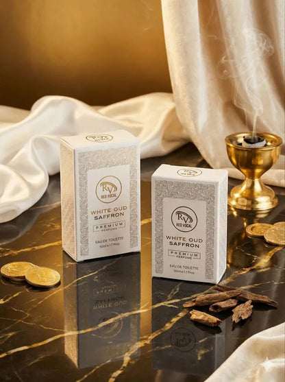 Two boxes of White Oud Saffron perfume on a reflective surface with gold coins and a candle. 
Red Vocal White Oud Saffron Premium Perfume Eau De Toilette 50ml – Luxury Fragrance For Unisex Set of 2