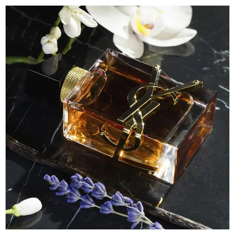Perfume bottle with gold cap on a dark surface with flowers Yves Saint Laurent Libre Eau de Parfum Intense 90 ml (3 fl.oz)